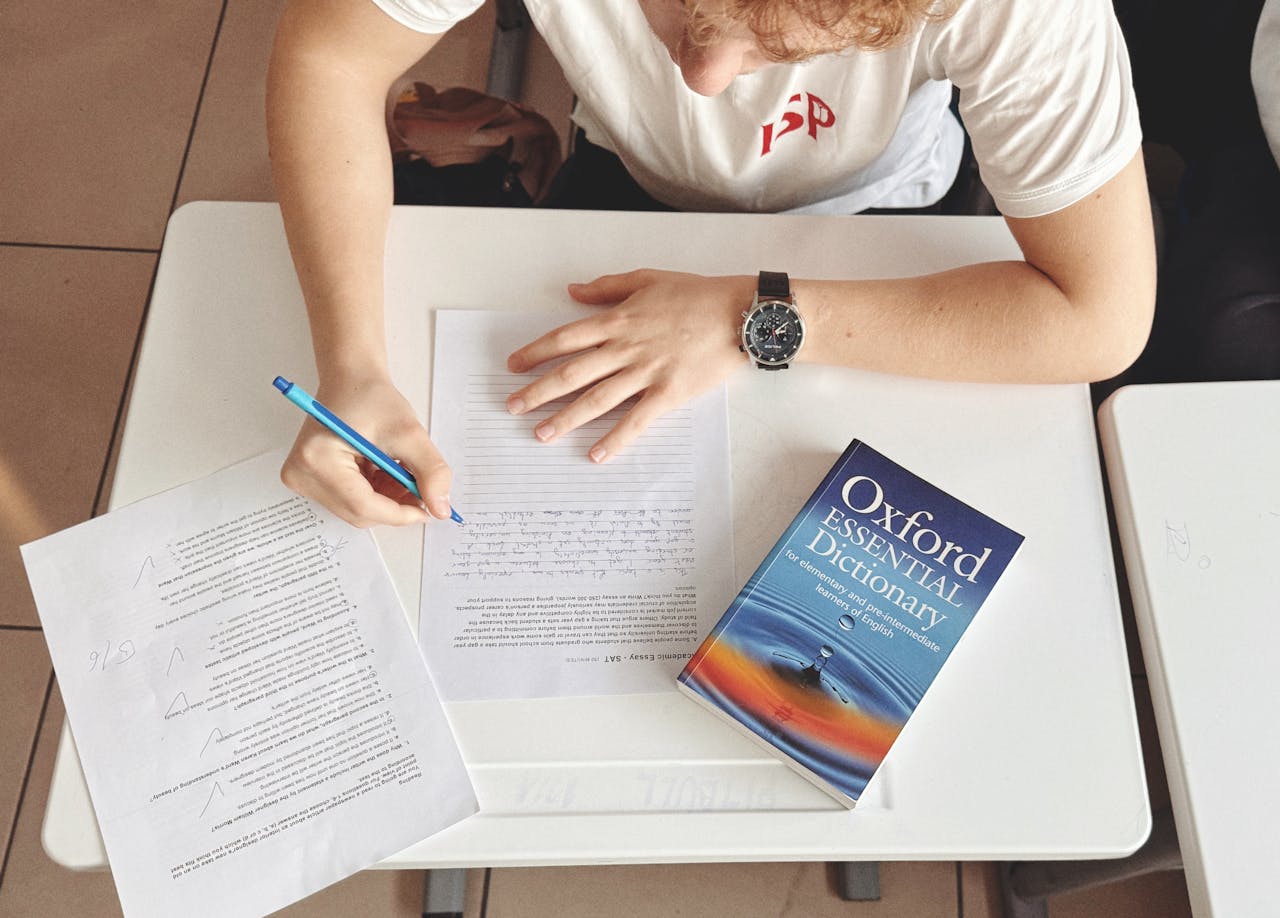 about-01 Student writing test using paper and Oxford dictionary on desk in classroom