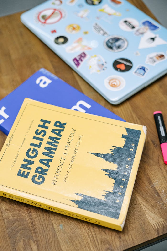 services-02 High-angle view of an English grammar book and a laptop with stickers on a wooden desk.