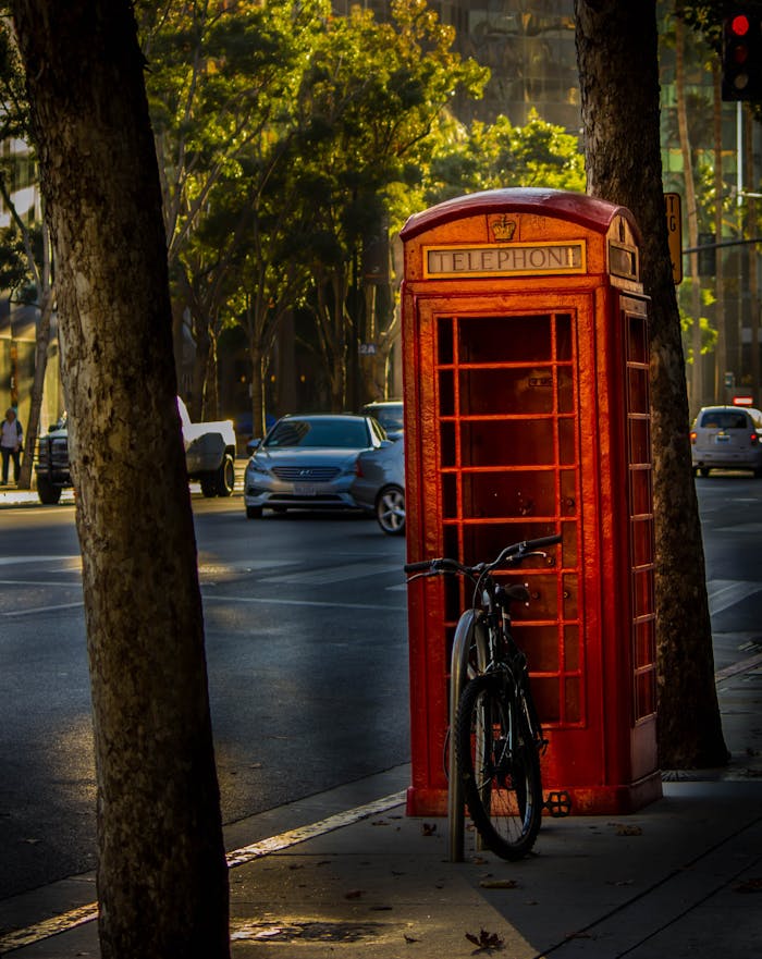 about-03 Vintage red telephone booth with bicycle in a vibrant urban setting at daytime.
